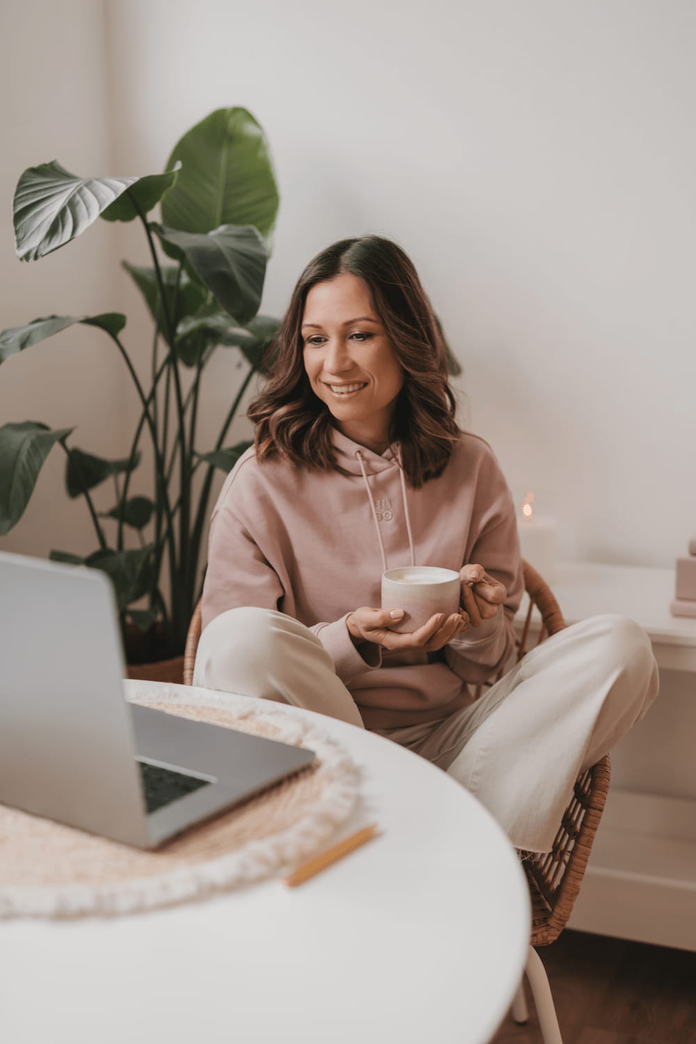 Frau sitzend vor dem Laptop mit Kaffee in der Hand