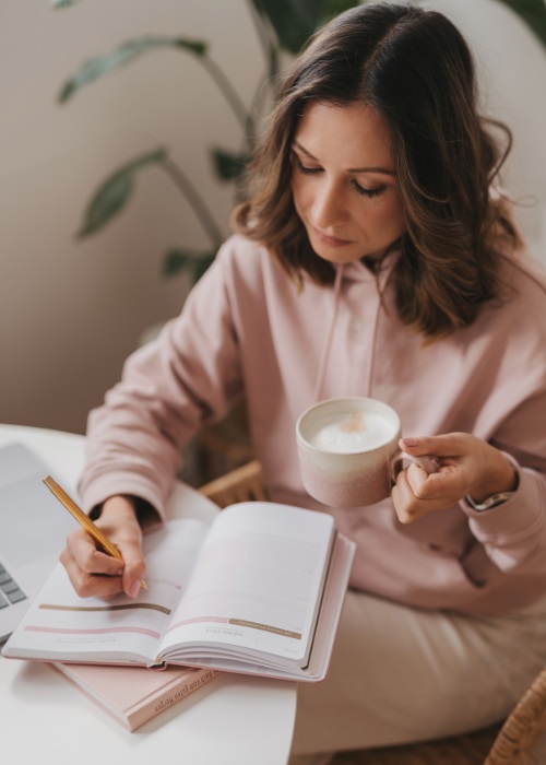 Webdesignerin macht nachdecklich Notizen in ihrem Notizbuch und hält eine Tasse in der Hand